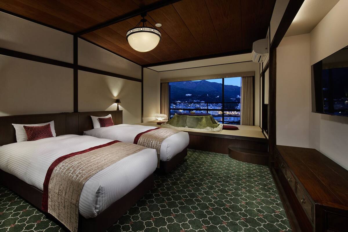 Ein Hotelzimmer mit zwei Betten, Blick auf die Stadt, einem großen Fenster und einer Holzbalkendecke.