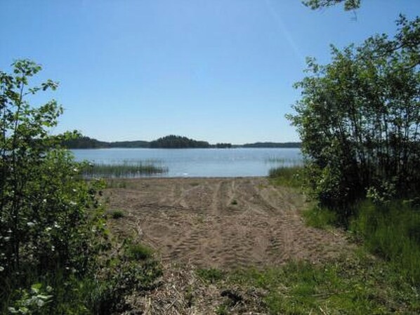 A sandy beach with a clear view of a lake and a distant island.