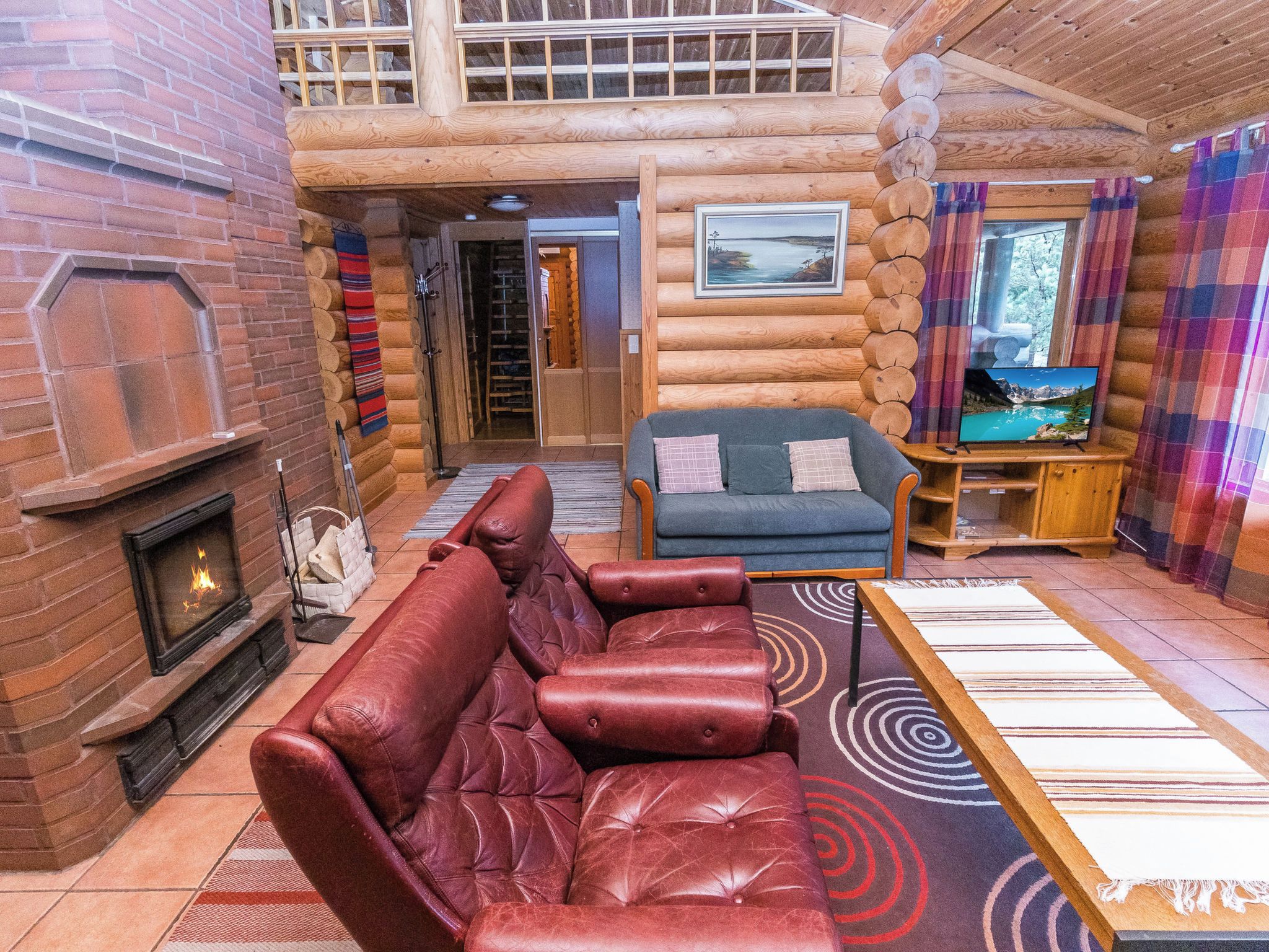 L'intérieur d'une cabane en rondins, avec une cheminée, un canapé en cuir et un téléviseur.