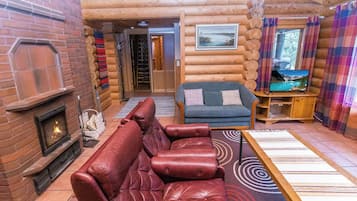 Ein Innenraum einer Blockhütte mit Kamin, Ledersofa und Fernseher.