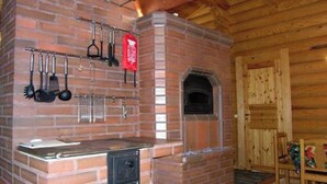 A brick kitchen with hanging utensils, a built-in oven, and a wooden dining area. - Metsämarja by Interhome (Kemiönsaari)