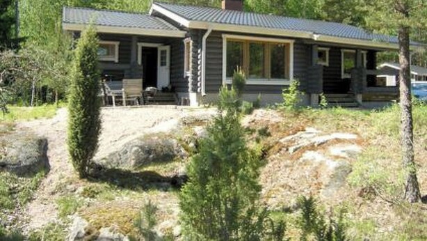 A two-story cabin with a covered porch and a chimney, surrounded by trees and a rocky landscape. - Metsämarja by Interhome (Kemiönsaari)