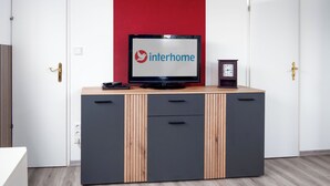 Ett modernt rum med en tv som visar Interhomes logotyp, en liten klocka och ett skåp med lådor.