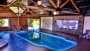 Ein großes Hallenbad mit Holzterrasse, Holzboden und einer großen Leinwand, die einen Wasserfall zeigt.