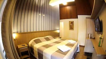Quarto de hotel com uma cama grande, uma mesa de cabeceira, um espelho, um quadro na parede e uma pequena mesa com um vaso de flores.