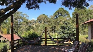 Eine Holzterrasse mit einer Hängematte und Korbstühlen, umgeben von Bäumen und blauem Himmel.