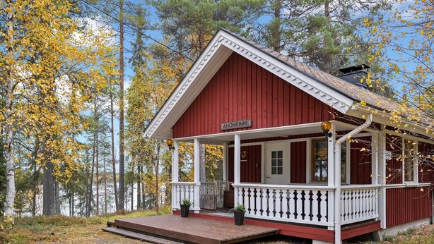 En rød træhytte med en hvid veranda og et skilt med teksten "AHONRINNE".
