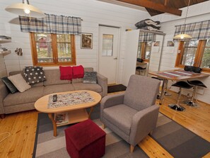 A cozy living room with a sofa, armchair, and coffee table, a kitchen area with a dining table, and a window with a view.