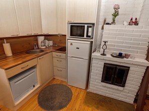 Cozy kitchen with a microwave, refrigerator, and sink, featuring a fireplace with decorative items on the mantel.