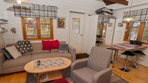 En hyggelig stue med sofa, lænestol og sofabord. Tjekkede gardiner, træloft og et vindue med udsigt.
