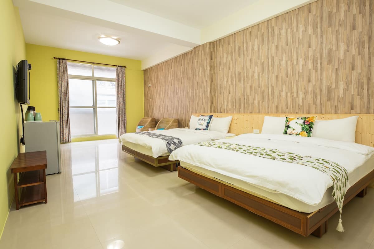 A hotel room with two beds, a wooden headboard, a flat-screen TV, and a window with curtains.