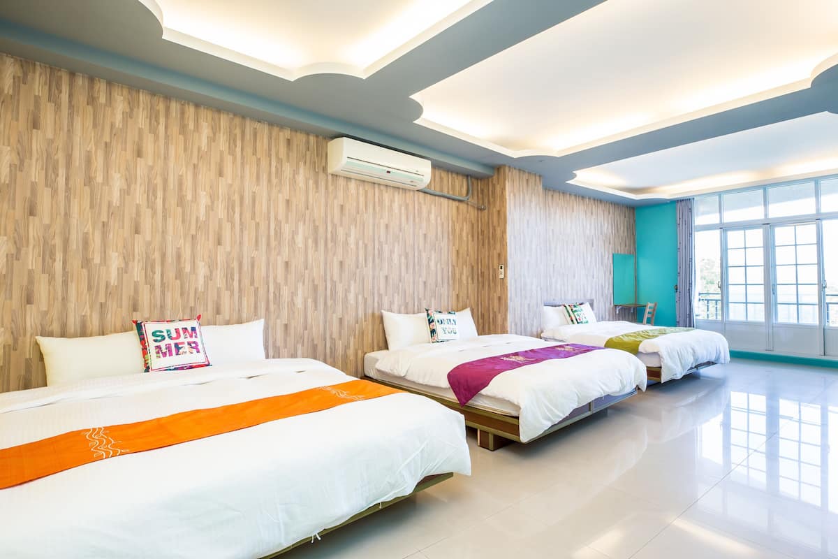 A hotel room with two beds, a wooden wall, an air conditioning unit, and large windows.