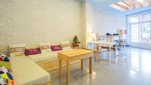 A modern living room with a white brick wall, a beige sofa with colorful cushions, a wooden coffee table, and a dining area with a table and chairs. - Green Stay (Hengchun)