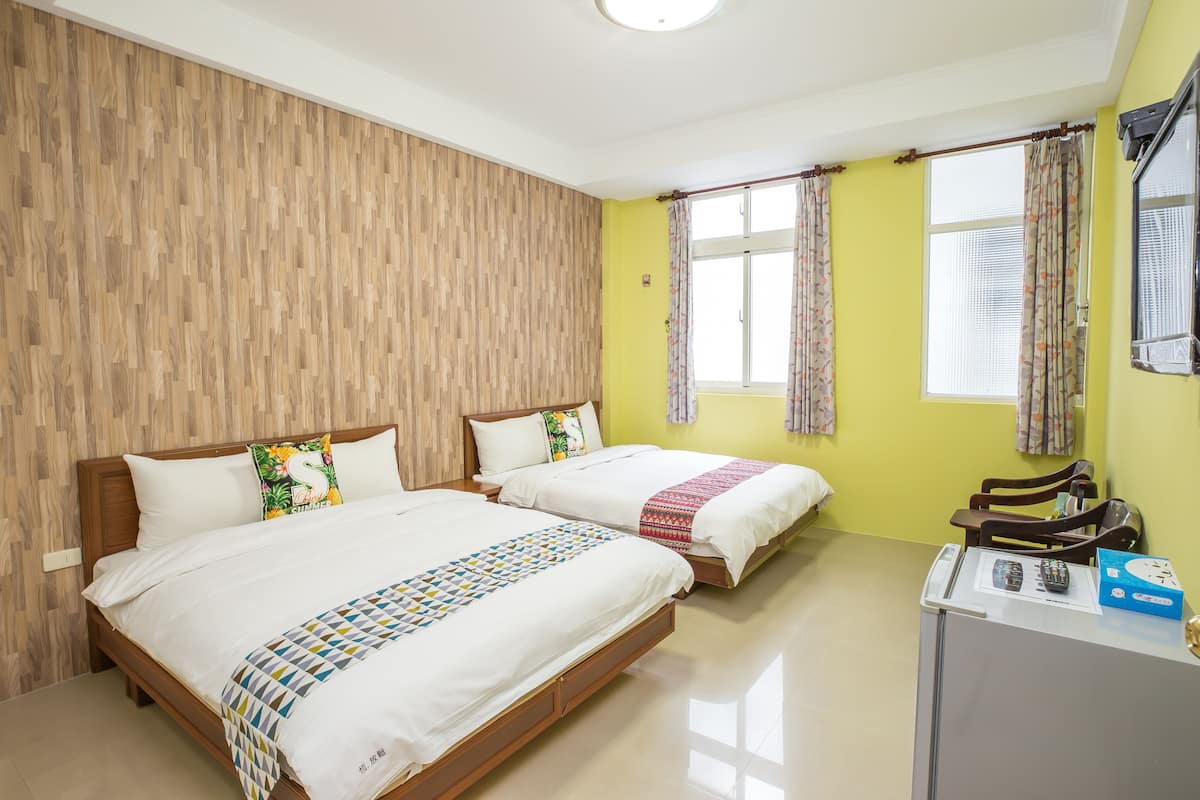 A hotel room with two beds, wooden headboard, yellow walls, and a small desk with a telephone and remote control.
