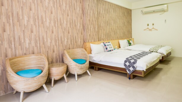 A bedroom with a wooden wall, a bed with white bedding, two wicker chairs with blue cushions, and an air conditioning unit on the wall. - Green Stay (Hengchun)