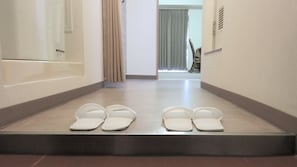A hotel hallway with a pair of slippers on the floor, a door with a mirror, and a window with curtains. - Sapporo Met S (Sapporo)