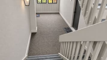 A staircase with a textured carpet leading to a landing with a door and windows.