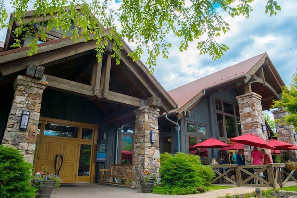 A rustic building with stone pillars, wooden beams, and a covered patio area with red umbrellas.