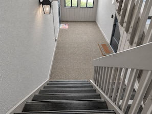 A staircase leading down to a carpeted area with a doormat and a wall-mounted light fixture.
