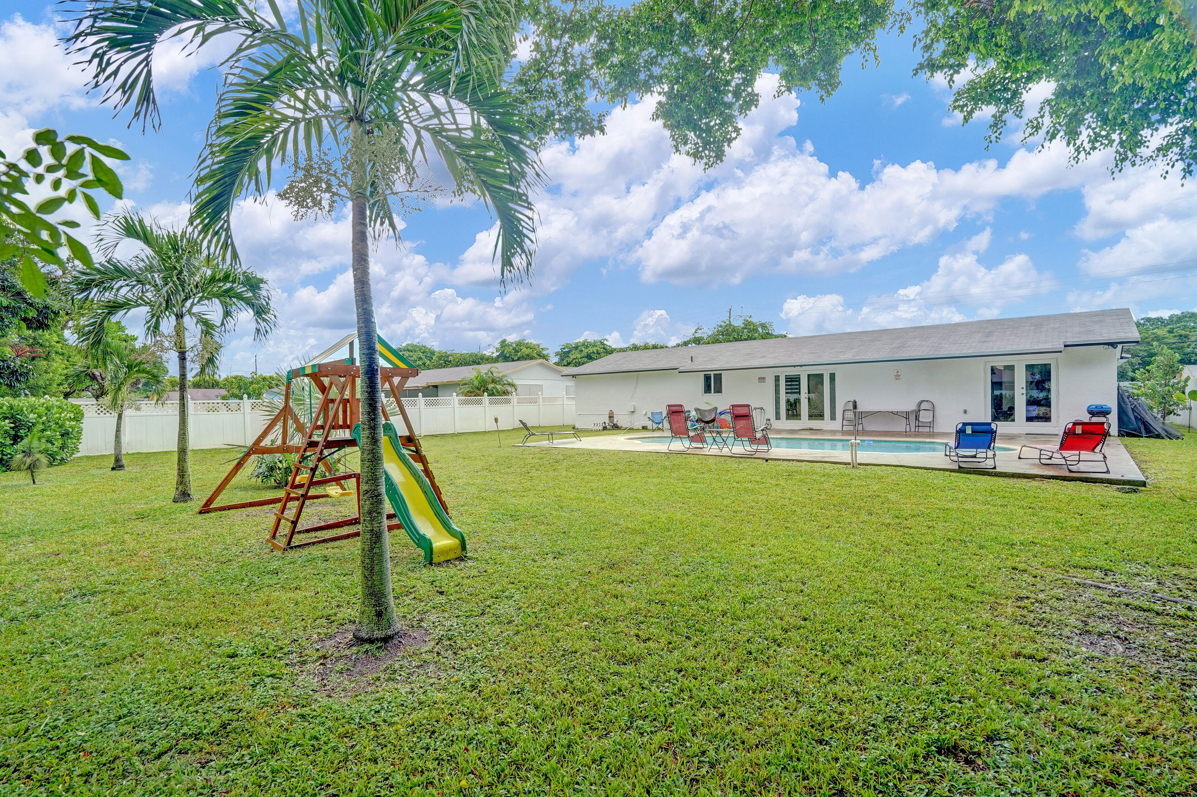 A backyard with a playset, a pool, and a building.