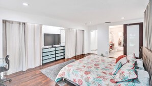A modern bedroom with a large bed, a TV, a desk, and a walk-in closet.