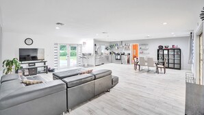 A modern living room with a grey sectional sofa, a flat-screen TV, and a dining area with chairs and a table.