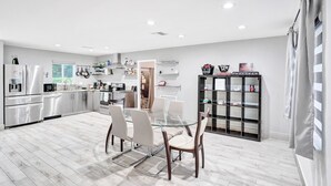 A modern kitchen with a glass dining table, stainless steel appliances, and a black shelving unit.