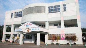 A modern building with a curved facade, multiple windows, and a prominent entrance with signage. - Kurion (Senboku)