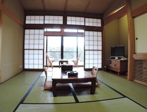 A tatami mat room with a low table, chairs, a television, and sliding doors. - Kurion (Senboku)