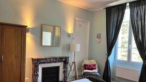 A bedroom with a bed, a wooden wardrobe, a fireplace, a chair, and a window with curtains. - STUNNING FRENCH HOUSE, SPACIOUS AND WELL EQUIPPED - SLEEPS 10 (Le Bourg-d'Oisans)