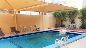 A swimming pool with lounge chairs and umbrellas, surrounded by a beige wall and greenery. - Sea view Serviced Apartment 2 bedroom 2 bath #1 (Hawally)