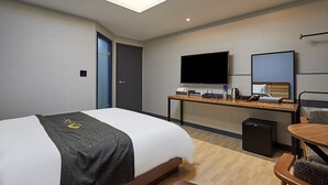 A hotel room with a bed, desk, TV, and a small refrigerator. - Gloa Hotel (Hwaseong)