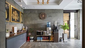 A modern hotel lobby with a reception desk, a large wall clock, a water dispenser, and a coffee machine. - Gloa Hotel (Hwaseong)