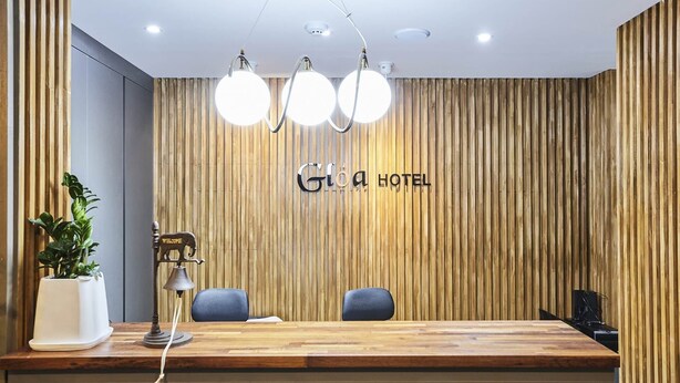 A reception desk with a wooden panel wall, a "Glia Hotel" sign, and two chairs. - Gloa Hotel (Hwaseong)