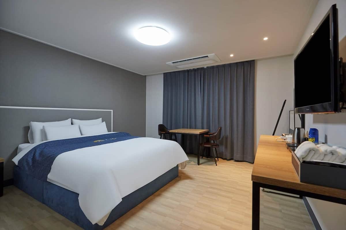 Hotellihuone, jossa on sänky, työpöytä, tuoli ja televisio.