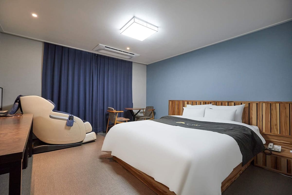 Hotellihuone, jossa on sänky, työpöytä, tuoli, ilmastointilaite ja yöpöytä, jossa on puhelin.