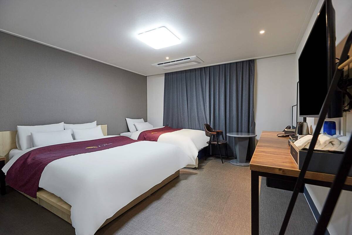 Hotellihuone, jossa on kaksi sänkyä, työpöytä, tuoli, taulutelevisio ja ikkuna, jossa on verhot.