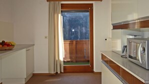 A compact kitchen with a microwave, a bowl of fruit on the counter, and a view through a wooden door to an outdoor area.