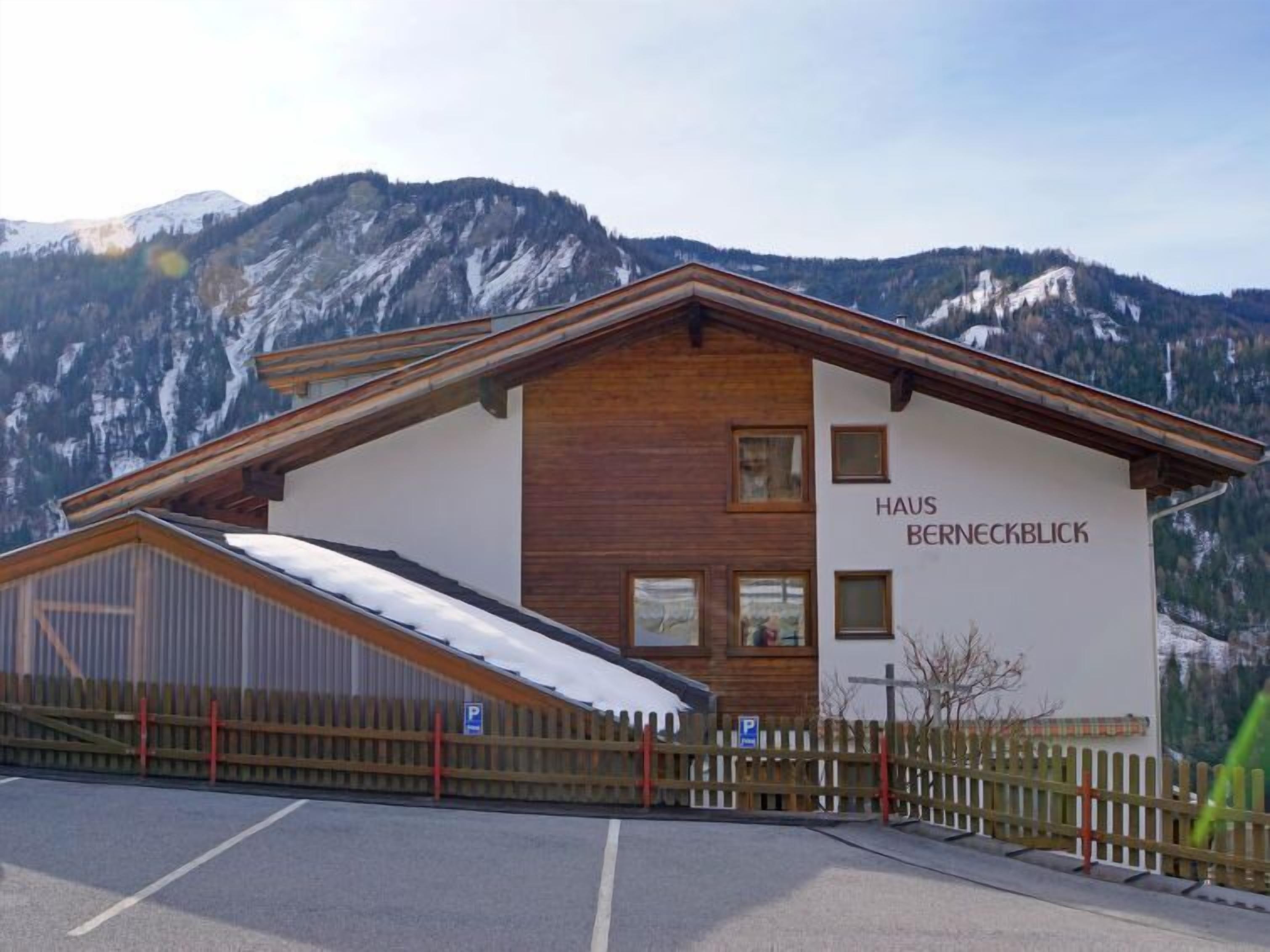 Ein Gebäude namens Haus Berneckblick mit einem geneigten Dach, einer Holzausfachung und Blick auf verschneite Berge im Hintergrund.
