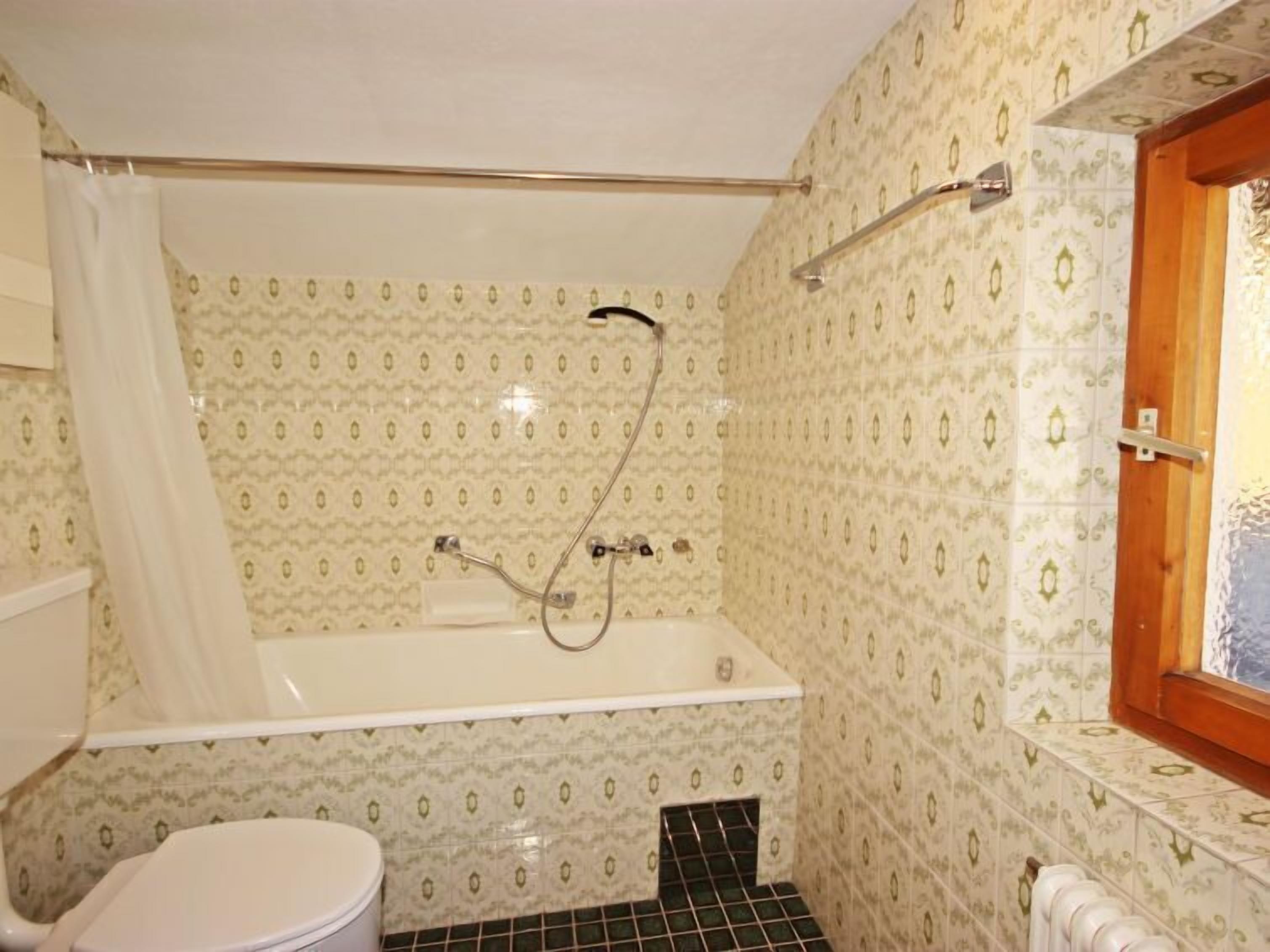 A bathroom with a bathtub, toilet, and a window.