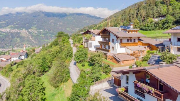 A hillside village with traditional wooden houses, a winding road, and a mountain backdrop.