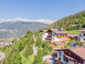 Un village perché sur une colline, avec ses maisons traditionnelles en bois, une route sinueuse et une chaîne de montagnes en toile de fond.