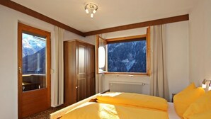 A hotel room with a bed, a wardrobe, a window with a mountain view, and a radiator.