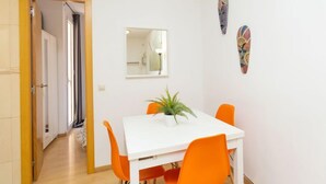 Ein Essbereich mit einem weißen Tisch, orangefarbenen Stühlen, einer Topfpflanze und zwei Wanddekorationen.