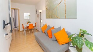 Ein modernes Wohnzimmer mit grauem Sofa, orangefarbenen Kissen, einem Esstisch mit Stühlen und einem großen, abstrakten Gemälde an der Wand.
