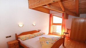 Un lit en bois dans une pièce dont le plafond est en pente, avec une petite table de chevet et une fenêtre avec des rideaux.