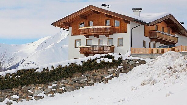 Un chalet à deux étages, doté de balcons en bois, qui se dresse sur fond de montagnes enneigées.