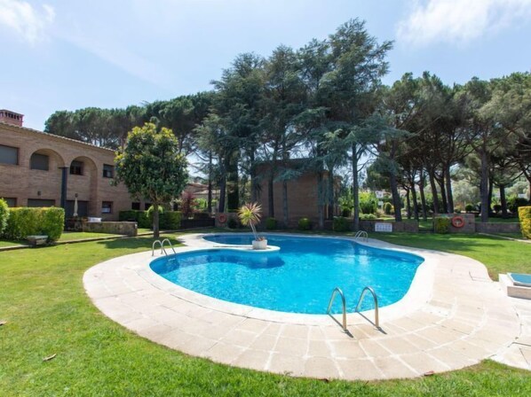 A swimming pool with a circular design, surrounded by a paved deck and a grassy area.