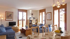 Un accogliente soggiorno con divano, tavolino e televisione. Sono presenti scaffali e un'area pranzo con tavolo imbandito per due persone.