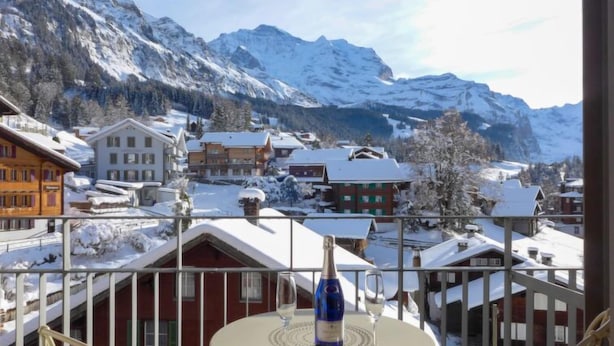 Un villaggio montano innevato con edifici tradizionali e un tavolo da balcone con una bottiglia e un bicchiere.